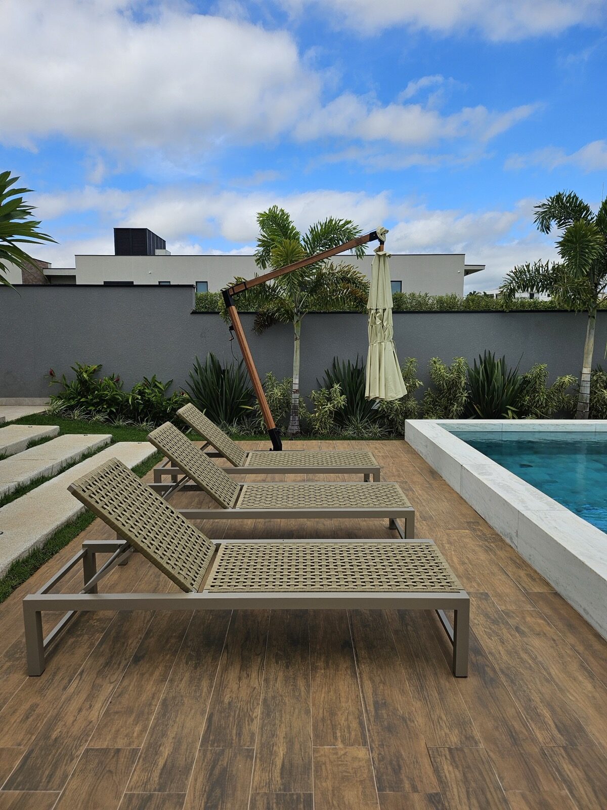 Sillas de mimbre y sombrillas de Mavie junto a una piscina residencial